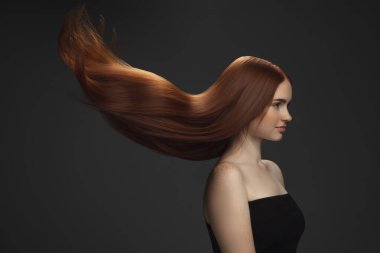 Koyu renk stüdyo arka planında uzun, düz, uçan kızıl saçlı güzel bir model..