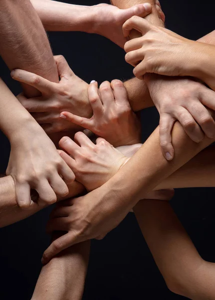 Las manos de la gente se agolpan en contacto aisladas en el fondo negro del estudio. Concepto de relación humana, comunidad, unidad, simbolismo — Foto de Stock