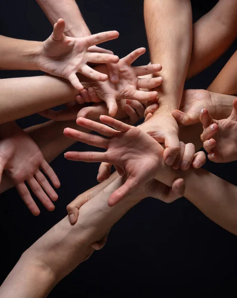 Las manos de la gente se agolpan en contacto aisladas en el fondo negro del estudio. Concepto de relación humana, comunidad, unidad, simbolismo — Foto de Stock