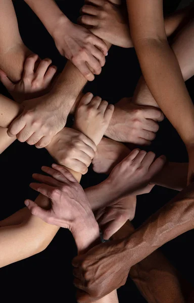 Las manos de la gente se agolpan en contacto aisladas en el fondo negro del estudio. Concepto de relación humana, comunidad, unidad, simbolismo — Foto de Stock