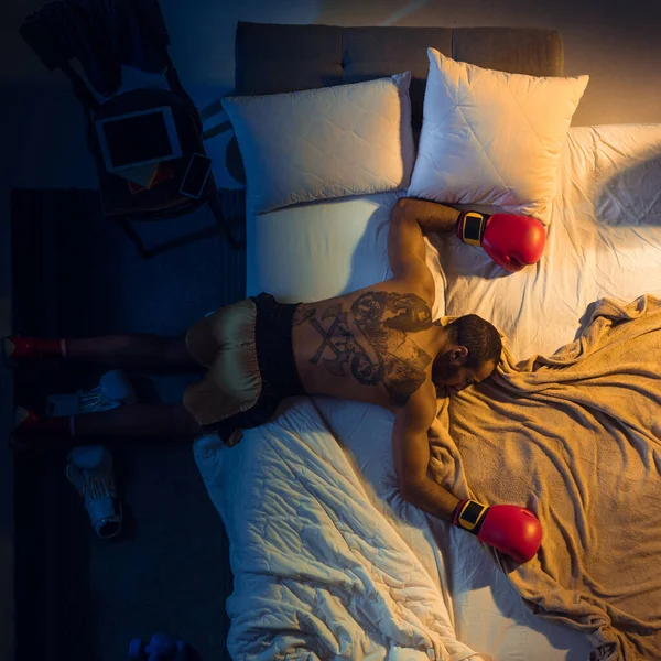 Вид сверху на молодого профессионального боксера, бойца, спящего в своей спальне в спортивной одежде с перчатками — стоковое фото