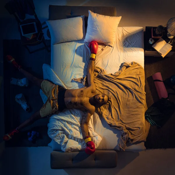 Vista superior del joven boxeador profesional, luchador durmiendo en su dormitorio en ropa deportiva con guantes —  Fotos de Stock