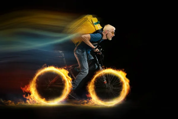 Быстрая доставка - курьер на велосипеде с заказом в огне на тёмном фоне — стоковое фото
