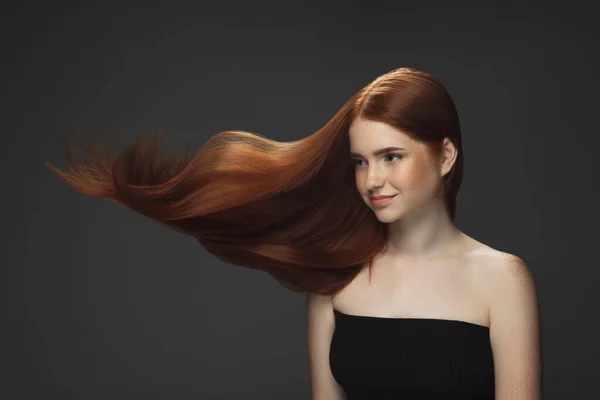 Beau modèle avec de longs cheveux rouges volants et lisses isolés sur fond de studio sombre. — Photo