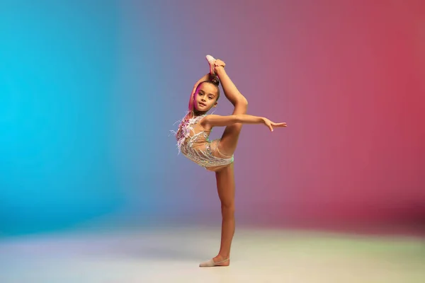 Niña caucásica, entrenamiento de gimnasta rítmica, realizando aislado en gradiente azul-rojo fondo del estudio en neón —  Fotos de Stock