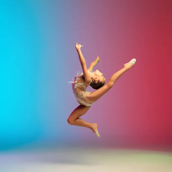 Liten kaukasiska flicka, rytmisk gymnast träning, utför isolerad på lutning blå-röd studio bakgrund i neon — Stockfoto