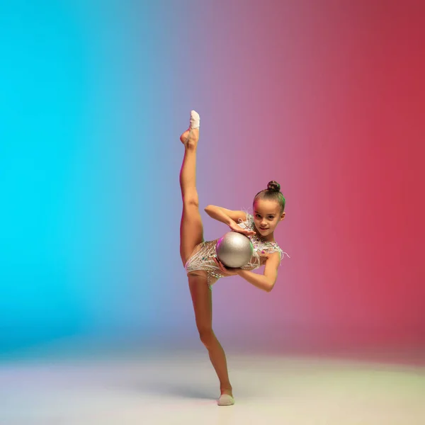 Piccola ragazza caucasica, allenamento ginnico ritmico, esibendosi isolata su sfondo gradiente blu-rosso in studio al neon — Foto Stock