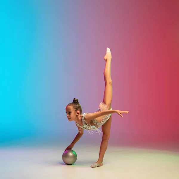 Piccola ragazza caucasica, allenamento ginnico ritmico, esibendosi isolata su sfondo gradiente blu-rosso in studio al neon — Foto Stock