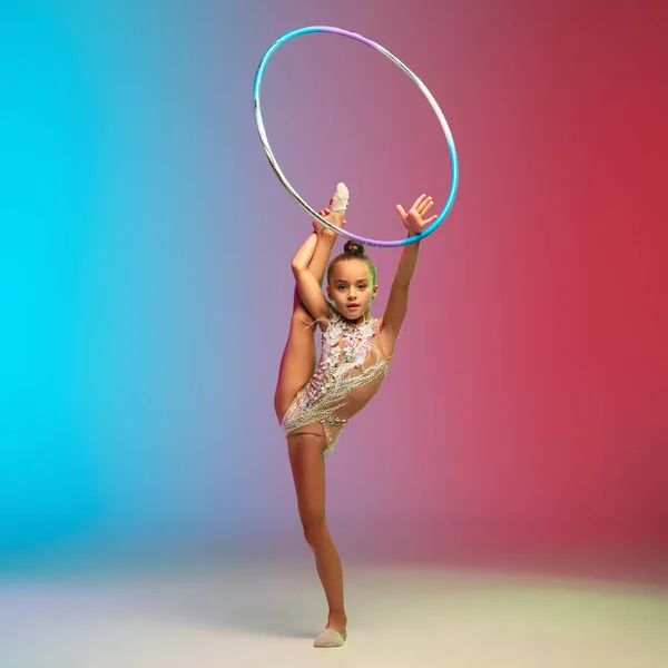 Liten kaukasiska flicka, rytmisk gymnast träning, utför isolerad på lutning blå-röd studio bakgrund i neon — Stockfoto