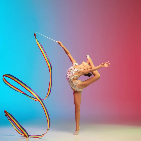 Klein blank meisje, ritmische gymnastiek training, het uitvoeren van geïsoleerd op gradiënt blauw-rode studio achtergrond in neon — Stockfoto