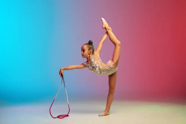 Niña caucásica, entrenamiento de gimnasta rítmica, realizando aislado en gradiente azul-rojo fondo del estudio en neón —  Fotos de Stock