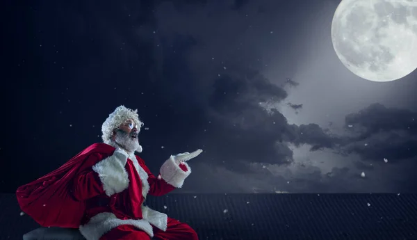 Duygusal Noel Baba yeni yıl ve Noel 'le kutluyor, gece yarısı dolunayda evin çatısında oturuyor. — Stok fotoğraf