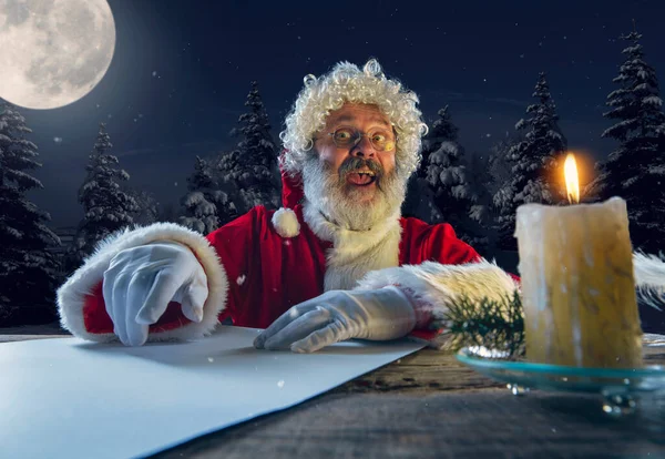 Duygusal Noel Baba yeni yıl ve Noel 'le kutluyor, bir mektup yazıyor, gece yarısı mum ile dilek listesi yapıyor. — Stok fotoğraf