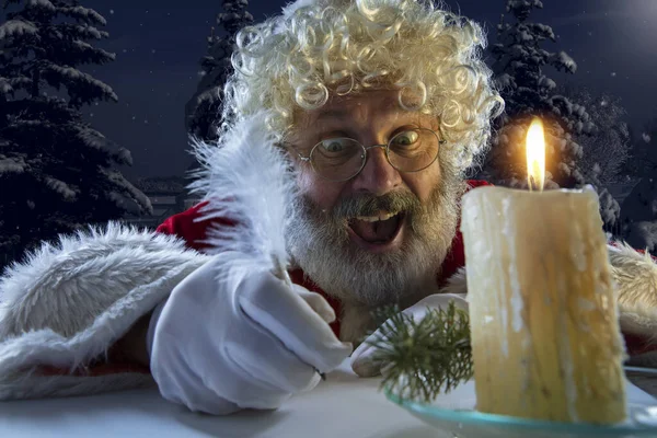 Babbo Natale emotivo congratulandosi con Capodanno e Natale, scrivendo una lettera, lista dei desideri a mezzanotte con candela — Foto Stock