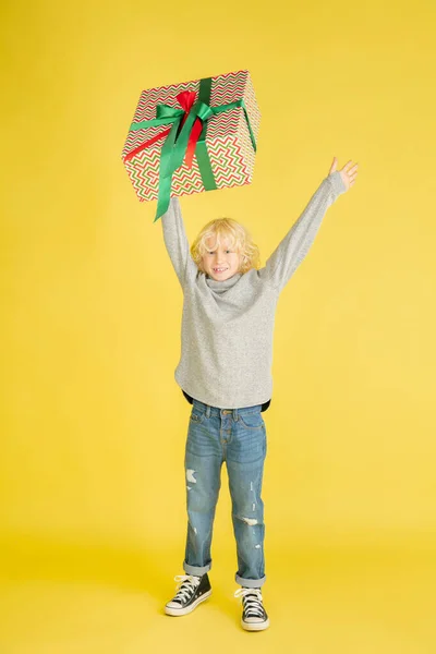 Ge och få presenter på julhelgen. Liten pojke som har kul isolerad på gul studio bakgrund — Stockfoto