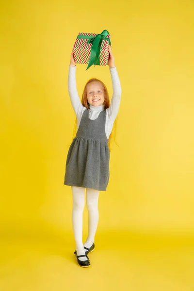 Giving and getting presents on Christmas holidays. Teen girl having fun isolated on yellow studio background — Stock Photo, Image