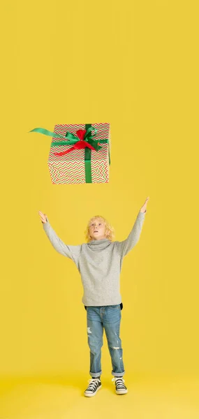 Dar e receber presentes nas férias de Natal. Menino se divertindo isolado no fundo do estúdio amarelo — Fotografia de Stock