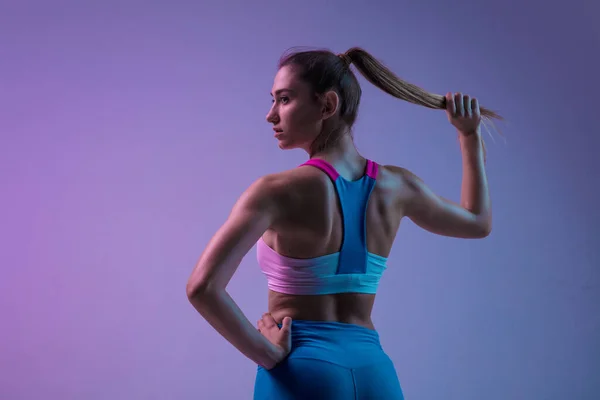 Jovem mulher esportiva treinando isolado no fundo do estúdio gradiente em luz de néon. atlético e gracioso — Fotografia de Stock