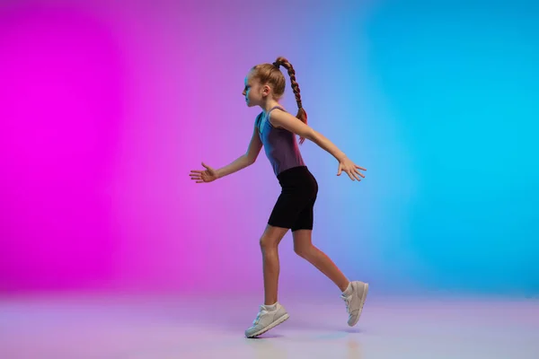 Tiener meisje lopen, joggen tegen gradiënt roze-blauw neon studio achtergrond in beweging — Stockfoto