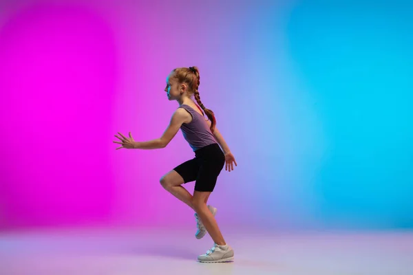 Tiener meisje lopen, joggen tegen gradiënt roze-blauw neon studio achtergrond in beweging — Stockfoto