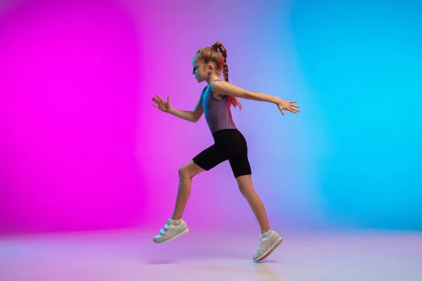 Tiener meisje lopen, joggen tegen gradiënt roze-blauw neon studio achtergrond in beweging — Stockfoto