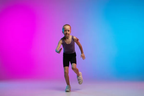 Tiener meisje lopen, joggen tegen gradiënt roze-blauw neon studio achtergrond in beweging — Stockfoto
