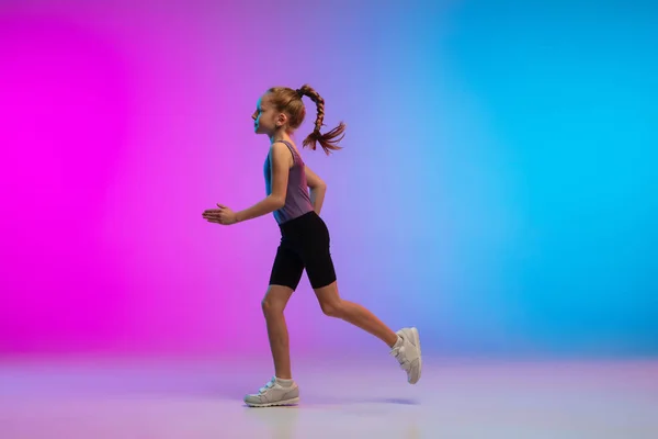 Teenagermädchen läuft, joggt gegen das Gefälle rosa-blauer Neon-Studiohintergrund in Bewegung — Stockfoto