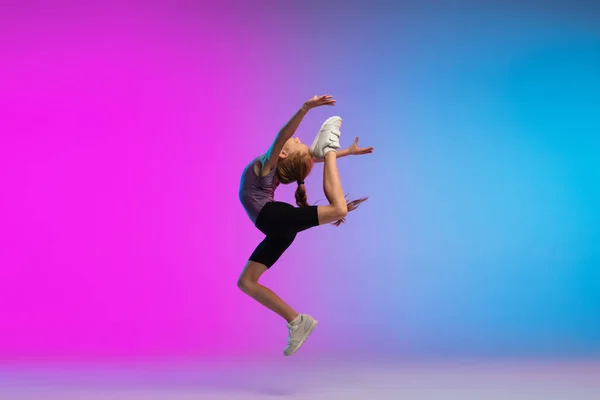 Teenage girl running, jogging against gradient pink-blue neon studio background in motion — Stock fotografie