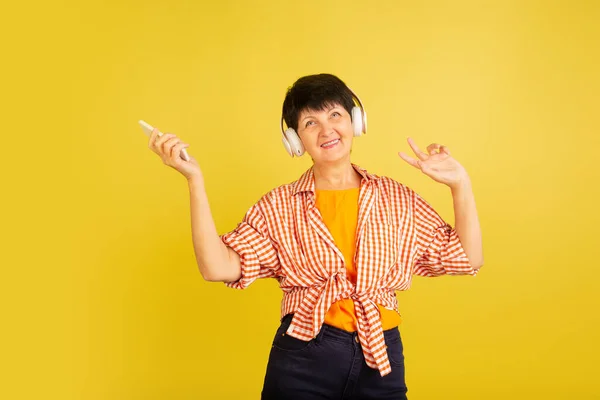 Mulher idosa isolada em fundo amarelo. Conceito de tecnologia e estilo de vida idoso alegre — Fotografia de Stock