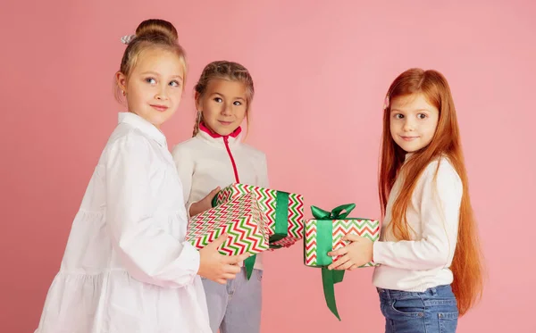 Подарки и подарки на рождественские праздники. Группа счастливых улыбающихся детей, получающих удовольствие изолированы на розовом фоне студии — стоковое фото
