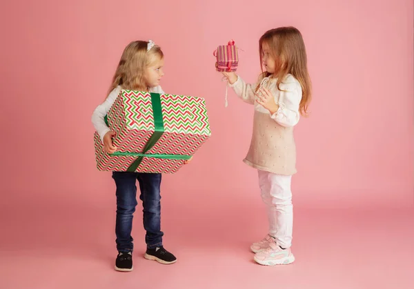 Dare e ricevere regali durante le vacanze di Natale. Due piccoli bambini sorridenti si divertono isolati su sfondo rosa — Foto Stock