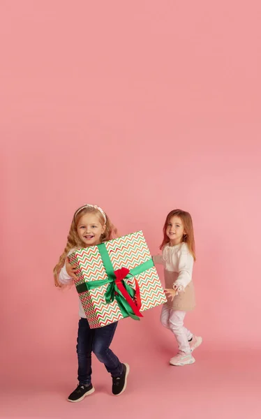 Dar e receber presentes nas férias de Natal. Duas pequenas crianças sorridentes se divertindo isoladas no fundo do estúdio rosa — Fotografia de Stock