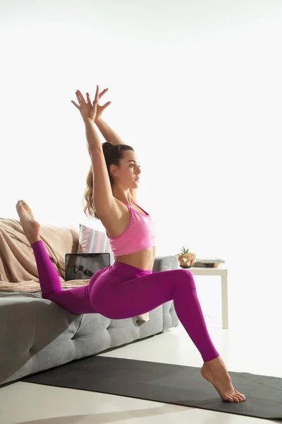 Hermosa mujer joven haciendo ejercicio en interiores, haciendo ejercicio de yoga en la alfombra gris en casa — Foto de Stock