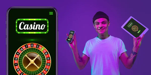 Juego en línea, concepto de casino. Joven sosteniendo dispositivos con lotería, cubierta de casino en luz de neón — Foto de Stock