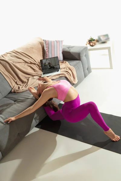 Mooie jonge vrouw uit te werken binnen, doen yoga oefening op grijze mat thuis — Stockfoto