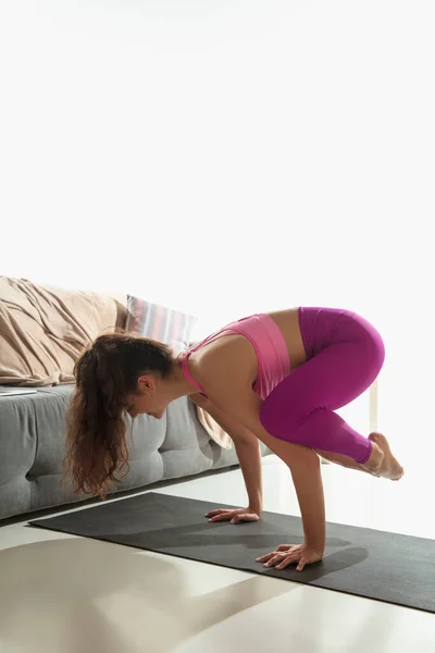 Hermosa mujer joven haciendo ejercicio en interiores, haciendo ejercicio de yoga en la alfombra gris en casa — Foto de Stock