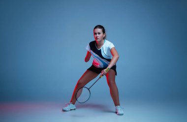 Badminton 'da pratik yapan güzel engelli kadın mavi arka planda neon ışıkta izole edilmiş.