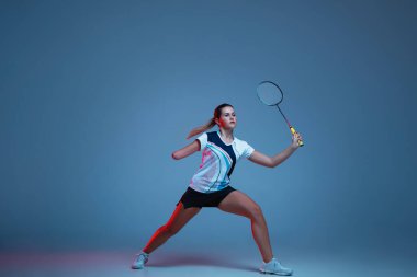Badminton 'da pratik yapan güzel engelli kadın mavi arka planda neon ışıkta izole edilmiş.