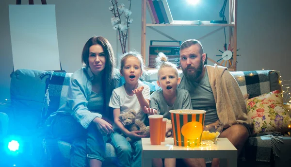 Família feliz assistindo projetor, TV, filmes com pipocas à noite em casa. Mãe, pai e filhos passam o tempo juntos. — Fotografia de Stock