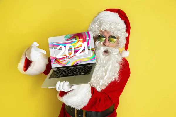 Elegante Santa Claus en traje tradicional con dispositivo moderno apuntando en 2021 sobre fondo de estudio amarillo — Foto de Stock