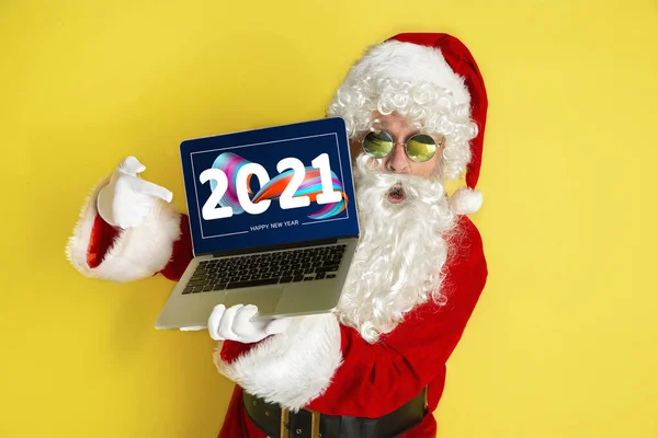 Elegante Santa Claus en traje tradicional con dispositivo moderno apuntando en 2021 sobre fondo de estudio amarillo — Foto de Stock
