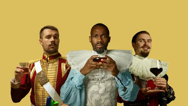 Średniowieczni mężczyźni jako członkowie rodziny królewskiej w klasycznej odzieży na żółtym tle. Koncepcja porównania epok, nowoczesności i renesansu. Kreatywny kolaż. — Zdjęcie stockowe
