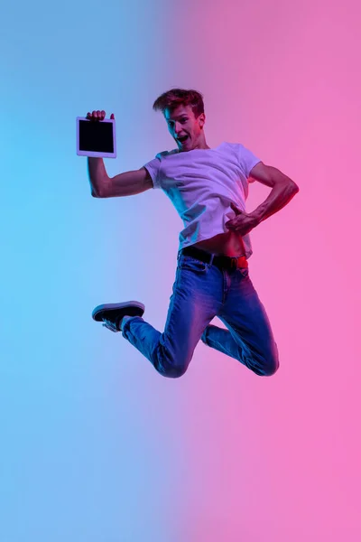 Giovane caucasico mans salto alto su gradiente blu-rosa studio sfondo in luce al neon — Foto Stock