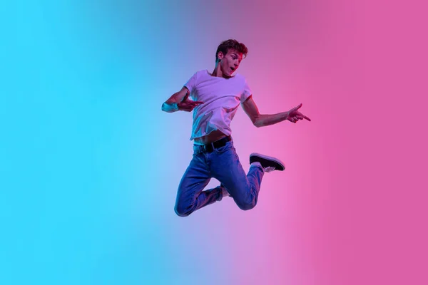 Jovens homens caucasianos pulando alto no gradiente azul-rosa estúdio fundo em luz de néon — Fotografia de Stock