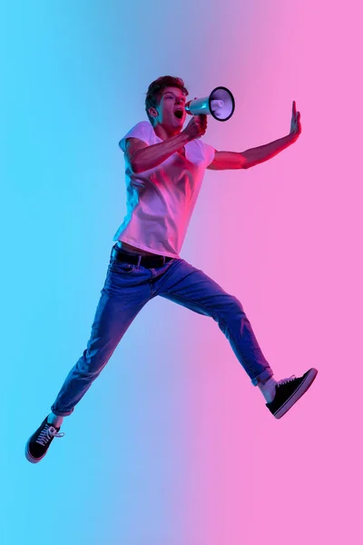 Jonge blanke mannen springen hoog op gradiënt blauw-roze studio achtergrond in neon licht — Stockfoto