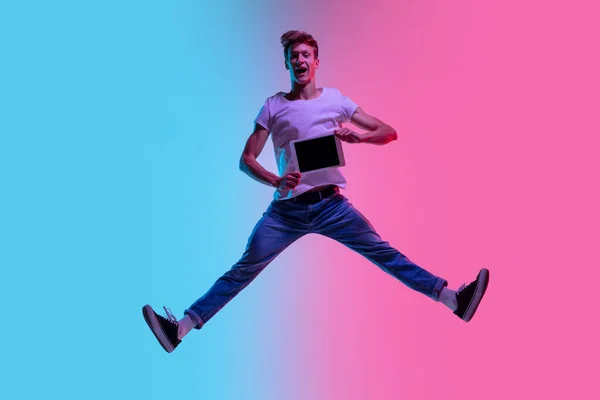 Young caucasian mans jumping high on gradient blue-pink studio background in neon light — Stock Photo, Image