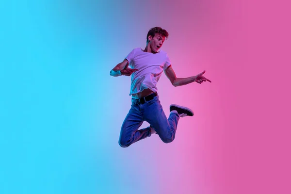 Young caucasian mans jumping high on gradient blue-pink studio background in neon light — Stock Photo, Image