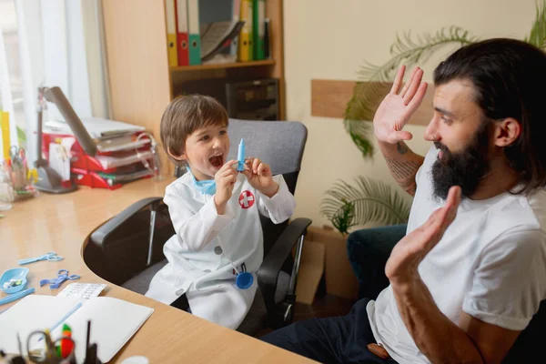 Menino brincando finge como médico examinando um homem no consultório médico comfortabe — Fotografia de Stock