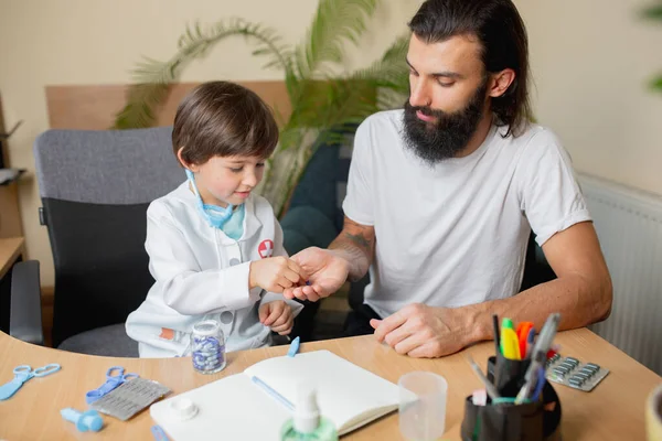 Kleine jongen spelen doet alsof als dokter onderzoeken van een man in comfortabele medische kantoor — Stockfoto