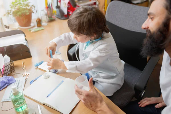 Kleine jongen spelen doet alsof als dokter onderzoeken van een man in comfortabele medische kantoor — Stockfoto